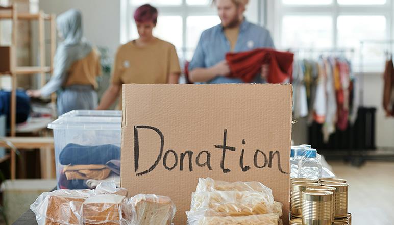 Donation box containing bread and canned goods, with volunteers sorting items at a food bank or charity organisation.