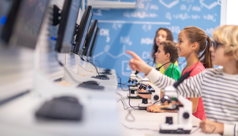 Students in a school computer lab using PCs and microscopes while collaborating on a STEAM learning activity.