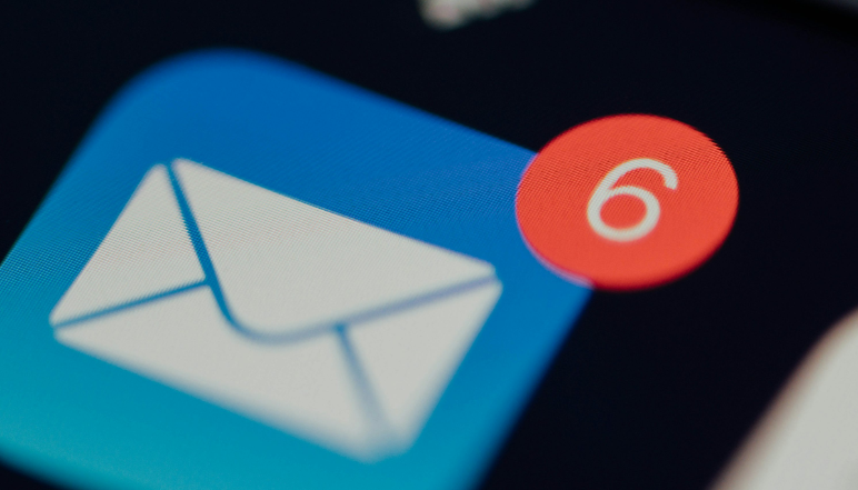 Close-up of a mobile phone showing an email app icon with a red notification badge indicating six unread messages, representing digital communication.