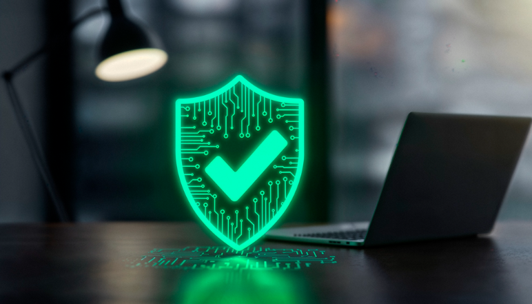 A glowing green shield icon with a white checkmark, representing cybersecurity or digital protection, in front of a laptop computer.